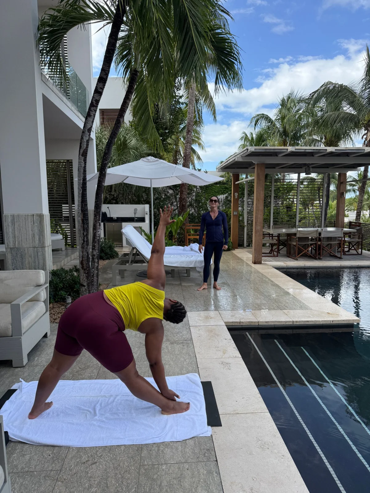 Woman doing yoga with an instructor beside a pool